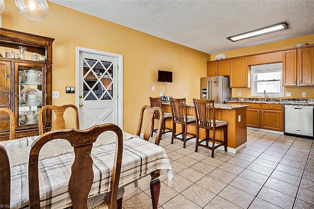 kitchen with brown cabinets, a breakfast bar area, light tile patterned floors, stainless steel appliances, and a textured ceiling