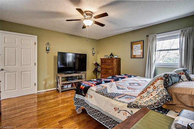 bedroom featuring ceiling fan, a textured ceiling, baseboards, and wood finished floors