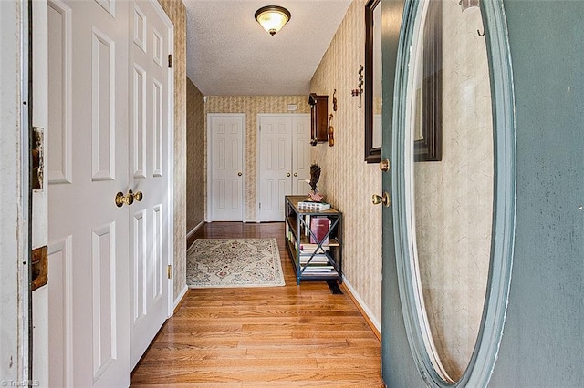 hallway with baseboards, light wood-style flooring, a textured ceiling, and wallpapered walls