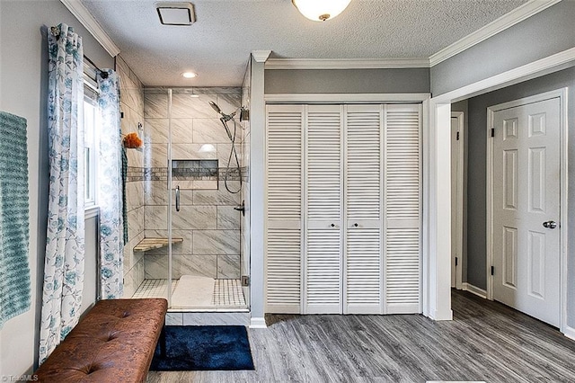 bathroom featuring a textured ceiling, a shower stall, wood finished floors, and crown molding