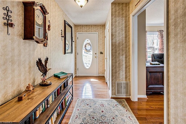 entryway featuring wallpapered walls, baseboards, visible vents, wood finished floors, and a textured ceiling