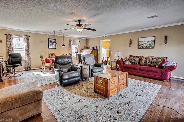 living area with ceiling fan, visible vents, baseboards, wood-type flooring, and crown molding