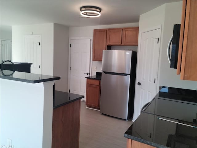 kitchen with a center island, stainless steel fridge, light wood-type flooring, and dark stone counters