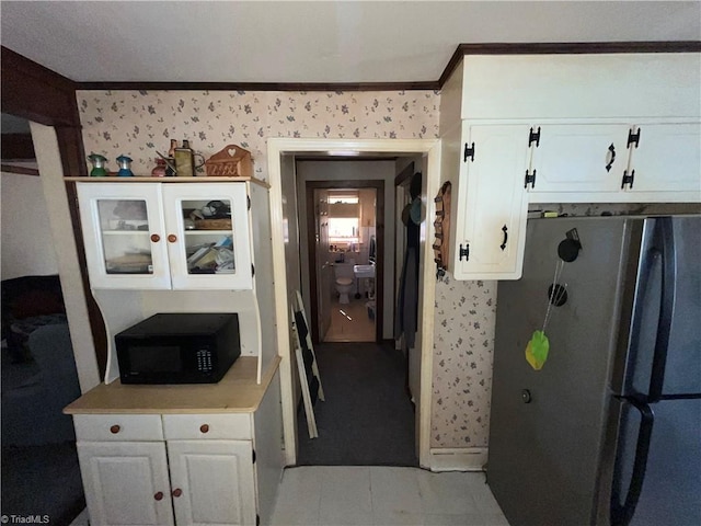 kitchen with white cabinetry, wallpapered walls, freestanding refrigerator, and black microwave