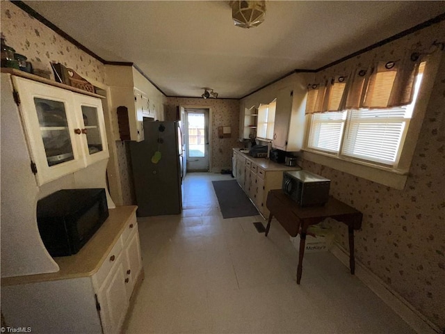 kitchen with wallpapered walls, white cabinets, black microwave, and freestanding refrigerator