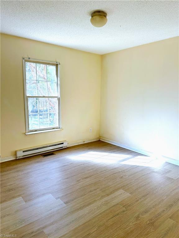 spare room with a textured ceiling, a baseboard heating unit, and wood finished floors