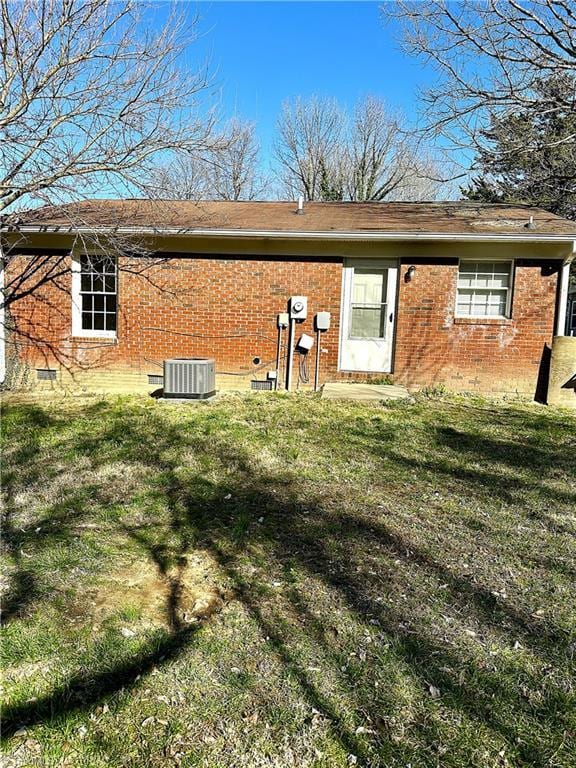 rear view of property featuring central air condition unit, a lawn, brick siding, and crawl space