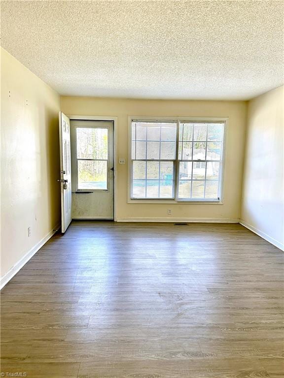 empty room with visible vents, a textured ceiling, baseboards, and wood finished floors