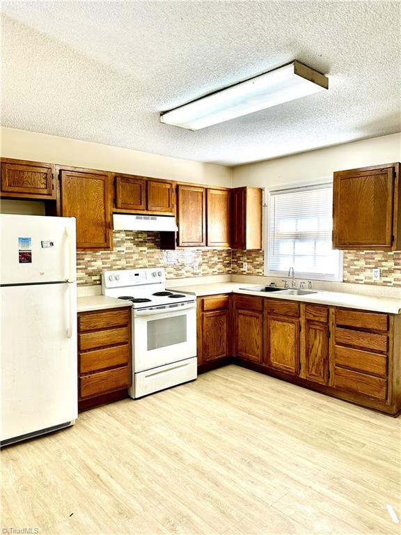 kitchen featuring white appliances, light wood-type flooring, under cabinet range hood, and brown cabinets