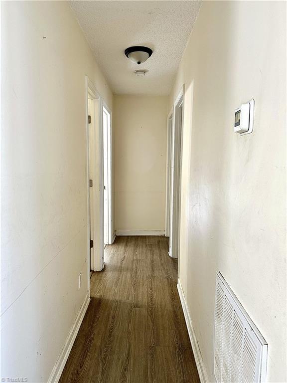 corridor with baseboards, wood finished floors, visible vents, and a textured ceiling