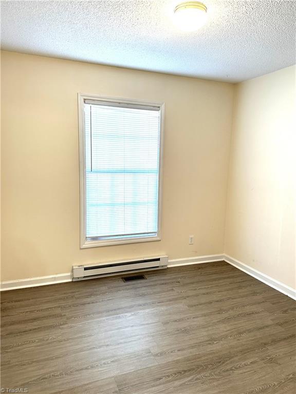 unfurnished room with a baseboard heating unit, dark wood finished floors, baseboards, and a textured ceiling