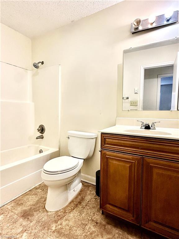 full bath featuring vanity, a textured ceiling, baseboards, shower / bath combination, and toilet