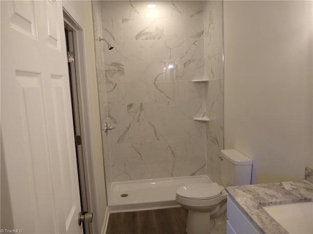 bathroom with hardwood / wood-style floors, vanity, toilet, and a tile shower