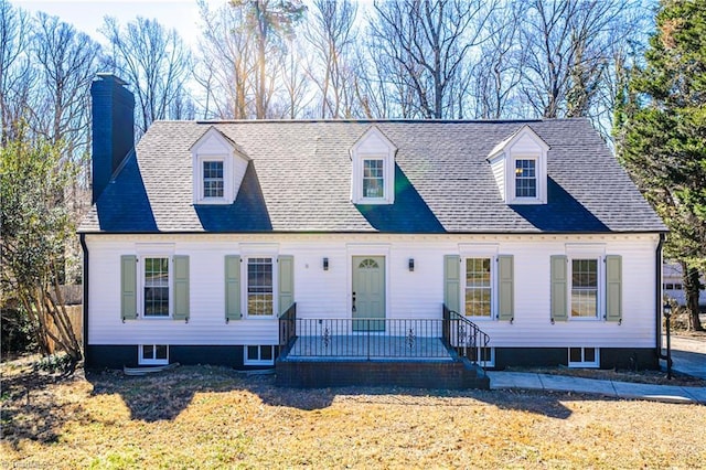 cape cod-style house featuring a chimney, roof with shingles, and a front yard