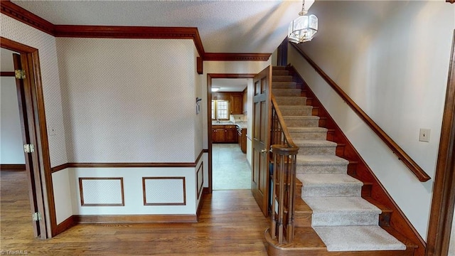 stairway featuring wood-type flooring, ornamental molding, and a textured ceiling