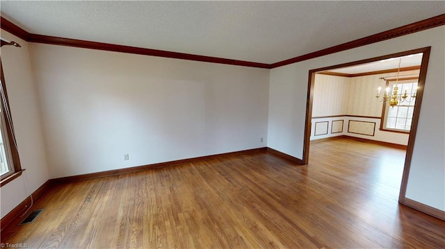 empty room featuring wood-type flooring, a chandelier, and crown molding