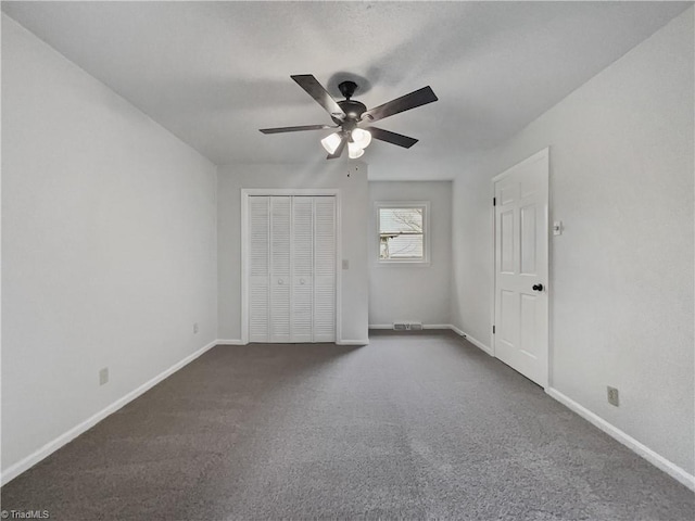 unfurnished bedroom with a closet, dark carpet, baseboards, and ceiling fan