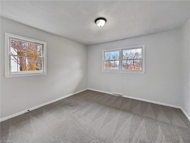 spare room featuring dark colored carpet, visible vents, a textured ceiling, and baseboards