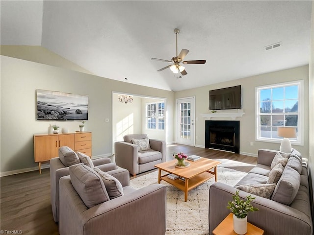 living area with lofted ceiling, a fireplace, wood finished floors, visible vents, and a ceiling fan