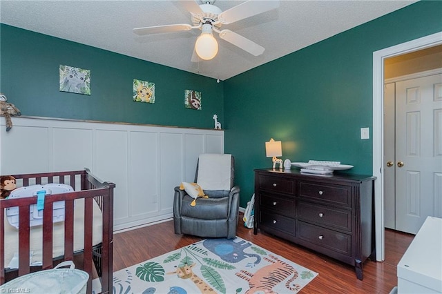 bedroom featuring wainscoting, ceiling fan, a crib, and wood finished floors