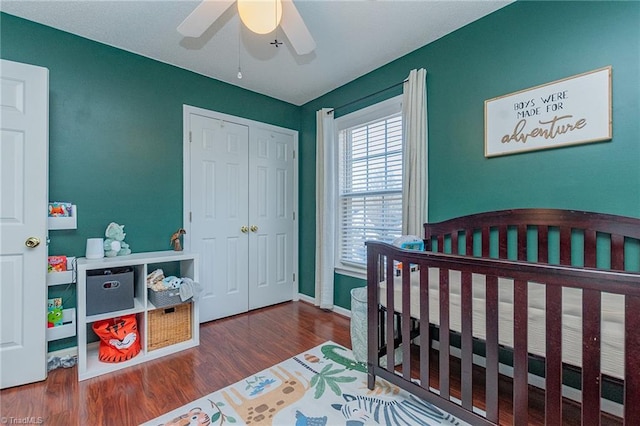 bedroom featuring wood finished floors, a ceiling fan, baseboards, a closet, and a crib