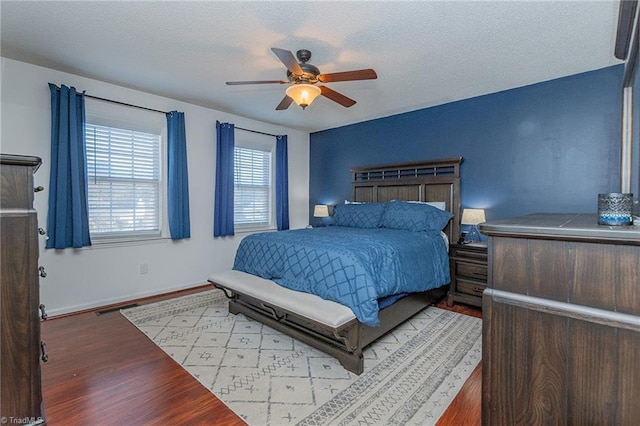 bedroom featuring ceiling fan, a textured ceiling, wood finished floors, visible vents, and baseboards