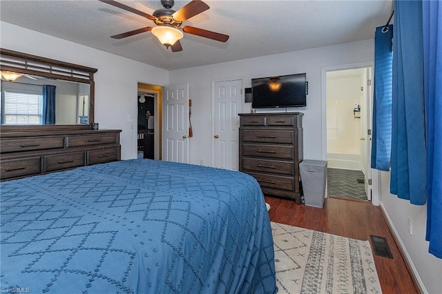 bedroom with connected bathroom, dark wood-type flooring, visible vents, baseboards, and a ceiling fan