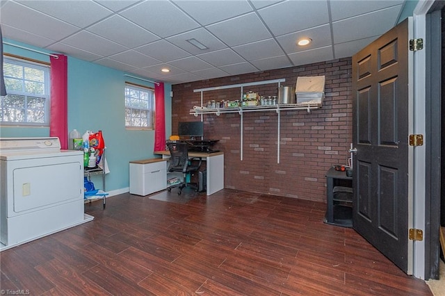 office space with a drop ceiling, brick wall, wood finished floors, baseboards, and washer / dryer