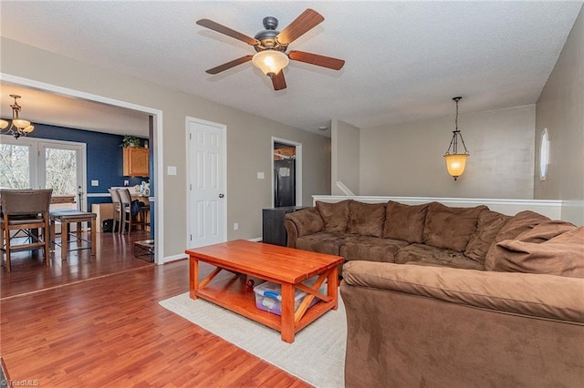 living area featuring ceiling fan with notable chandelier, baseboards, and wood finished floors