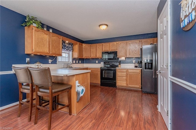 kitchen with dark wood finished floors, a breakfast bar area, a peninsula, light countertops, and black appliances