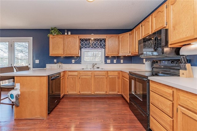 kitchen with a sink, black appliances, a peninsula, and light countertops