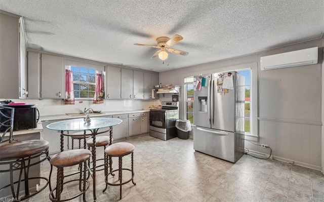 kitchen featuring plenty of natural light, a wall unit AC, stainless steel appliances, and ceiling fan