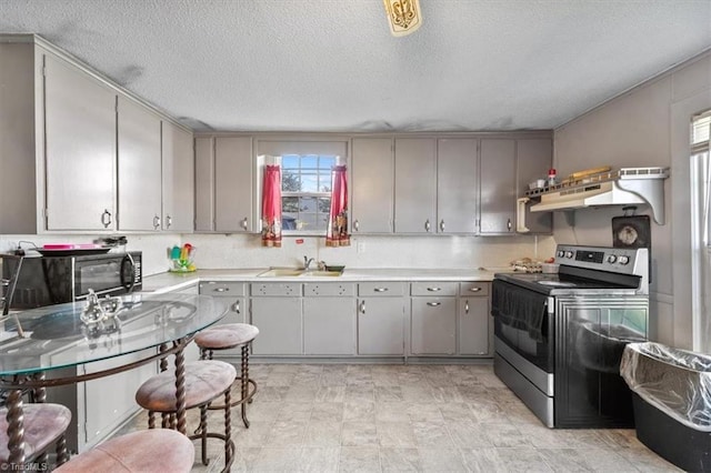 kitchen with a textured ceiling, gray cabinetry, stainless steel electric range oven, sink, and ventilation hood