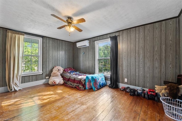 bedroom with wood-type flooring, a wall unit AC, ceiling fan, and wooden walls