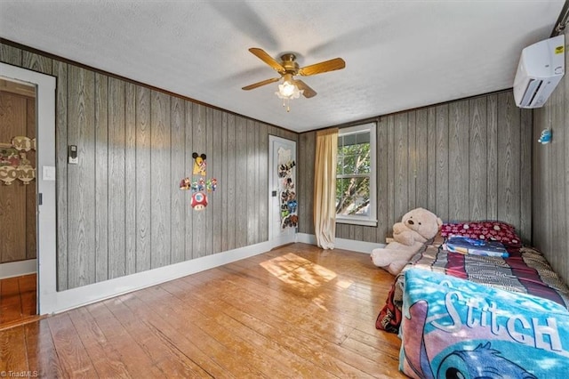 bedroom with hardwood / wood-style flooring, a wall unit AC, ceiling fan, and wooden walls