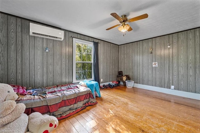 bedroom featuring ceiling fan, wood walls, an AC wall unit, and hardwood / wood-style flooring