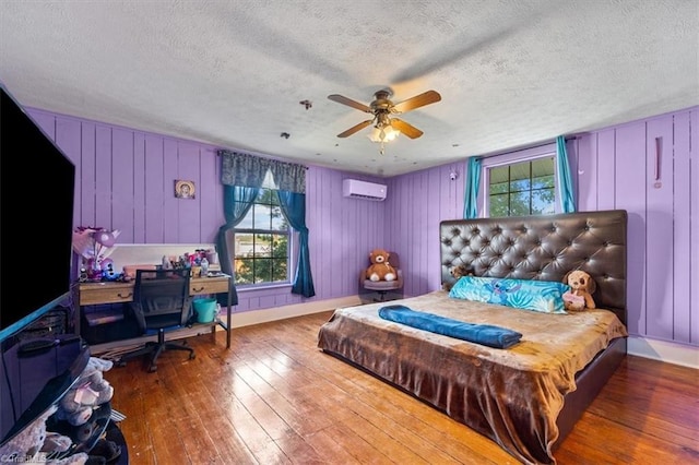 bedroom featuring hardwood / wood-style floors, multiple windows, a wall unit AC, and ceiling fan