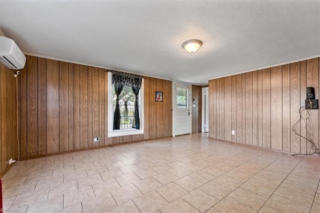 empty room featuring a textured ceiling, a wall unit AC, wooden walls, and light tile patterned flooring