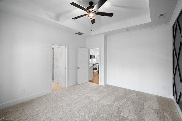 unfurnished bedroom featuring crown molding, a tray ceiling, light colored carpet, and ceiling fan