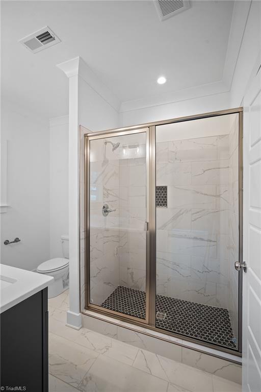 bathroom featuring an enclosed shower, vanity, ornamental molding, and toilet