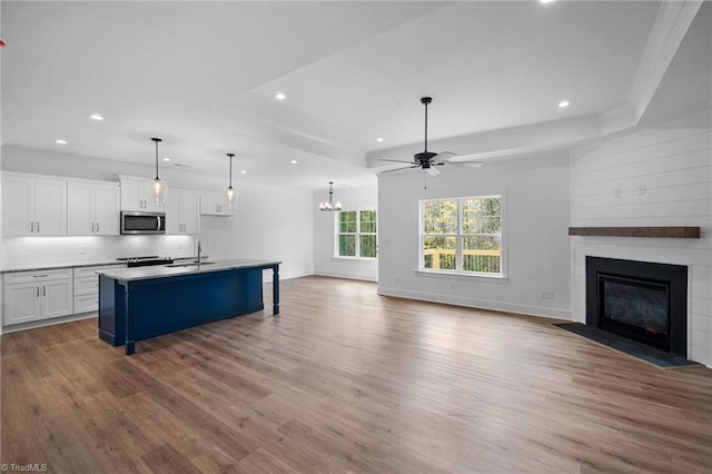 kitchen with white cabinetry, sink, a large fireplace, a kitchen bar, and a center island with sink