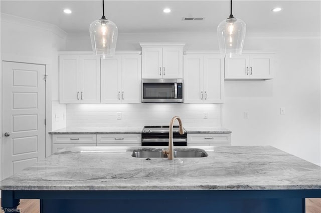 kitchen featuring pendant lighting, stainless steel appliances, an island with sink, and white cabinets