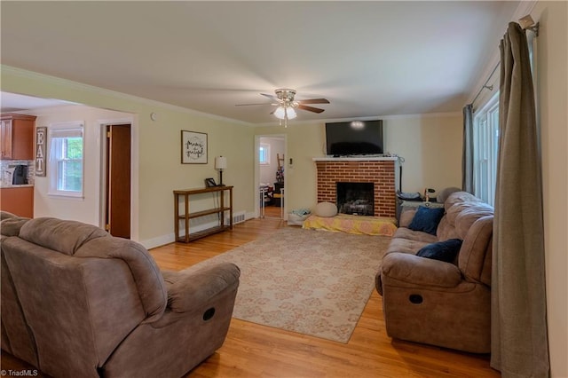 living area with a ceiling fan, light wood-type flooring, baseboards, ornamental molding, and a brick fireplace
