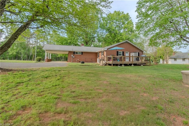 back of property featuring a carport, brick siding, a deck, a yard, and aphalt driveway