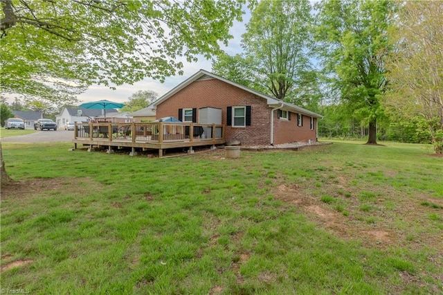 rear view of house with a wooden deck, a lawn, and brick siding