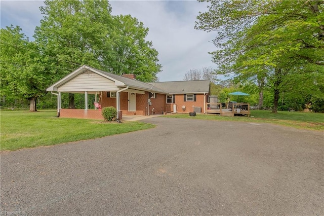 ranch-style house featuring a front lawn, driveway, a chimney, brick siding, and a deck