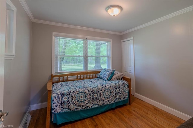 bedroom with wood finished floors, a closet, baseboards, and ornamental molding