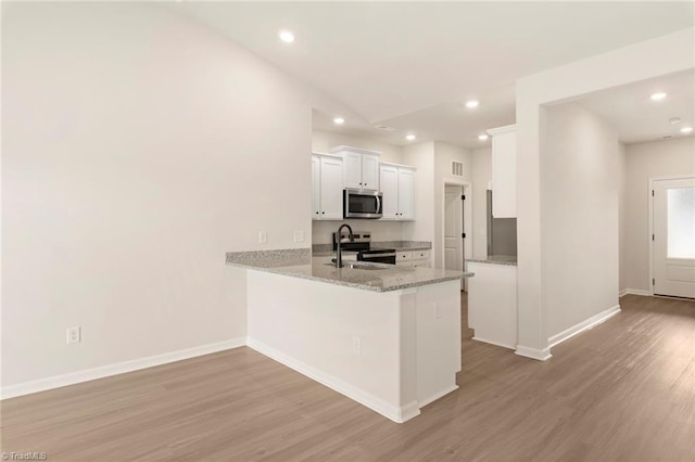 1047 Russell Dr, Winston-Salem, NC 27127 - kitchen featuring a sink, white cabinetry, a peninsula, light wood-style flooring, and stainless steel appliances