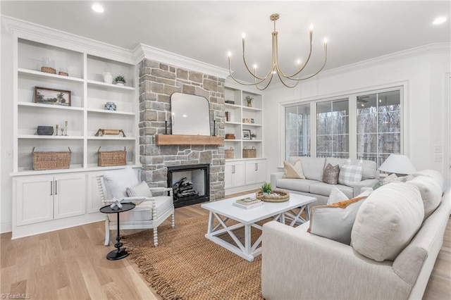 living area featuring built in features, an inviting chandelier, ornamental molding, a stone fireplace, and light wood-type flooring