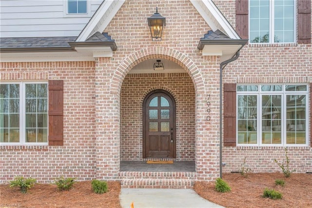 property entrance featuring a shingled roof and brick siding